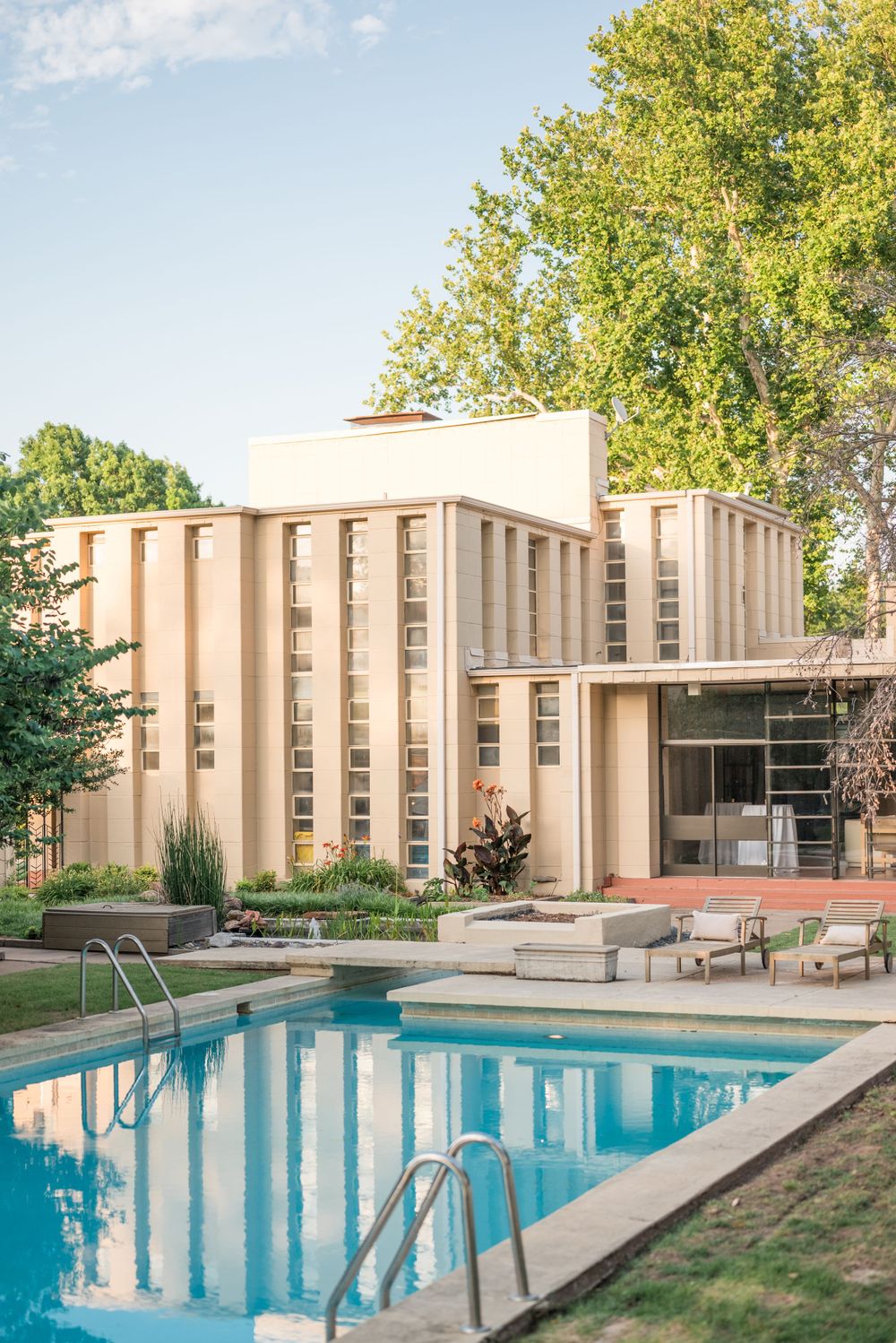 Mid-century modern building with swimming pool and lounge chairs surrounded by lush greenery.