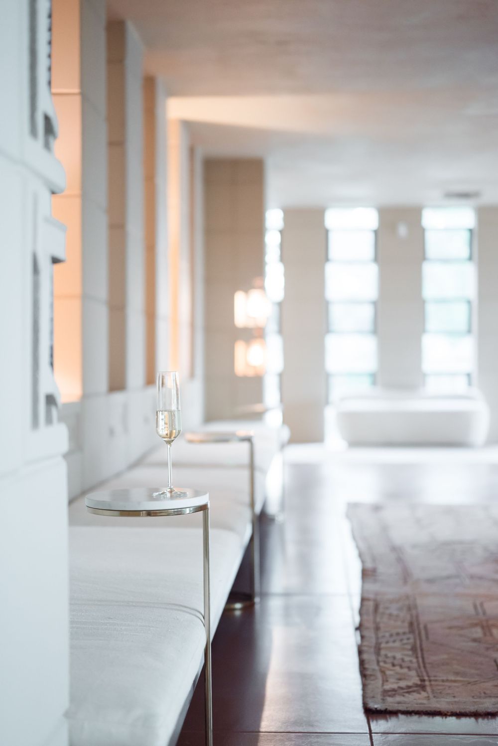 Minimalist white hallway with elegant glassware and furniture bathed in natural sunlight.