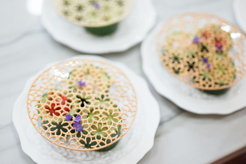 Delicate floral cookies on white plates with intricate lace-like patterns and pastel colors.