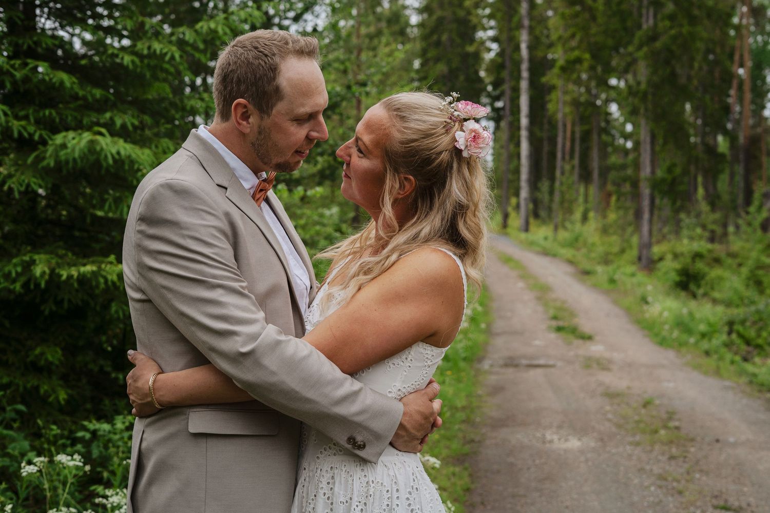 Brudpar som kramas på en skogsstig under sin bröllopsfotografering i Ockelbo.