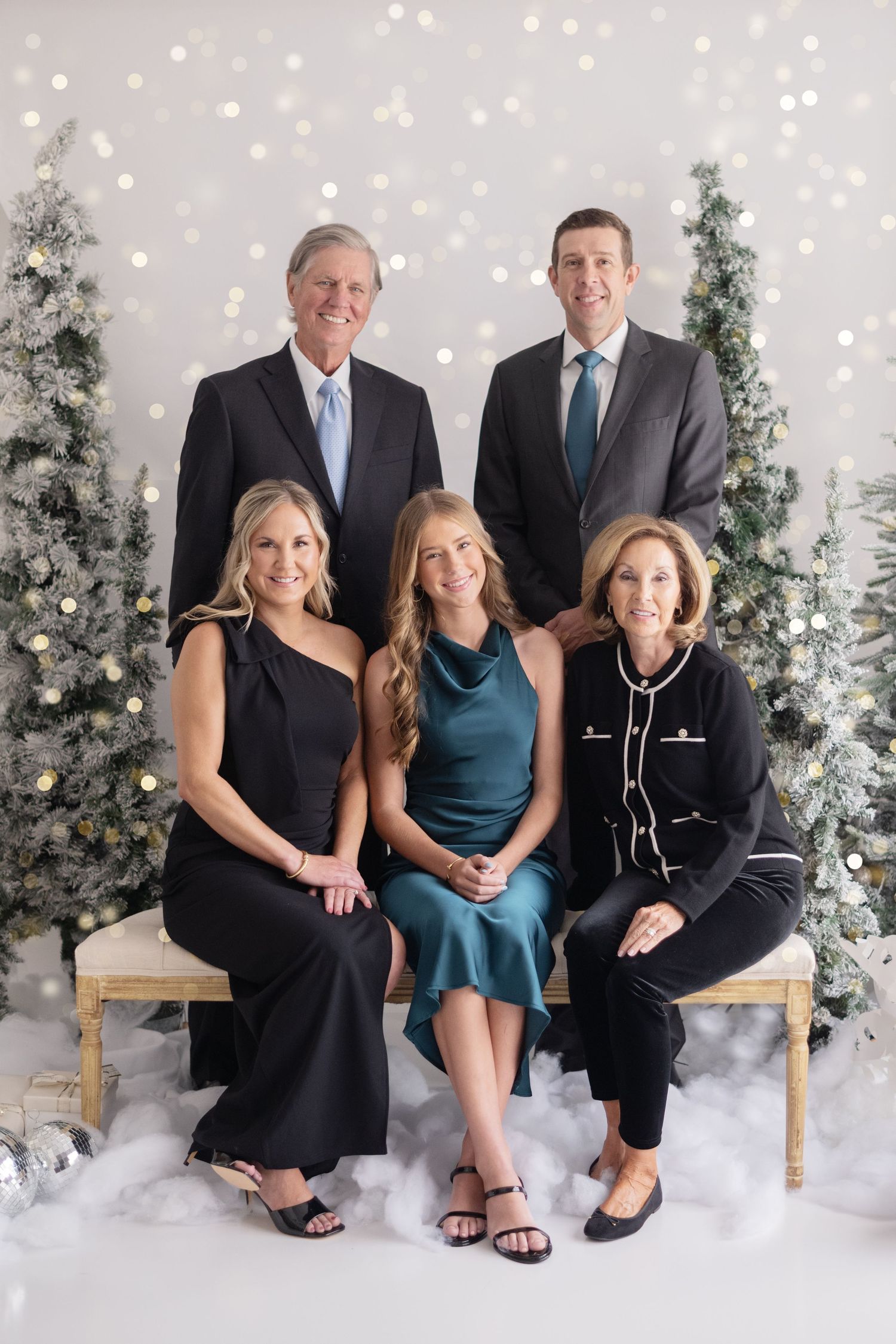 Family of five posing for a festive Christmas portrait surrounded by snow-flocked trees and warm bokeh lights.