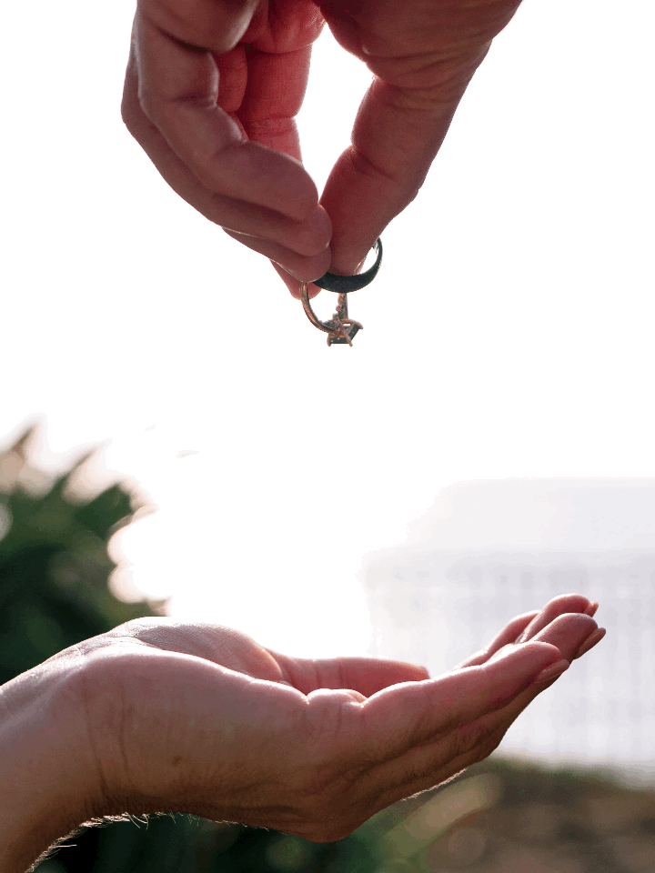 Two hands exchanging a diamond engagement ring against a bright outdoor background.