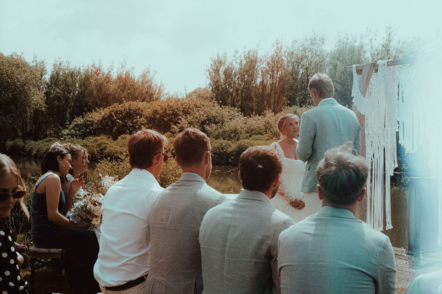 Outdoor wedding ceremony with guests seated, bride and groom standing at altar with lush greenery backdrop.