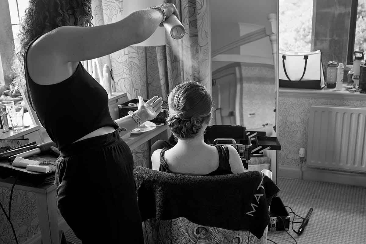 Black and white photo of a hairstylist styling a bridesmaid at Dalston Hall wedding venue