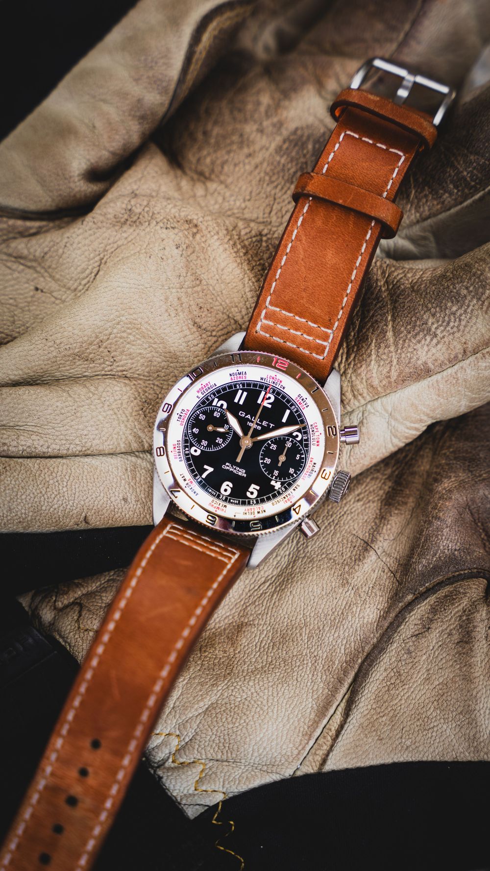 Hamilton chronograph watch with black dial on tan leather strap, displayed on worn leather gloves.