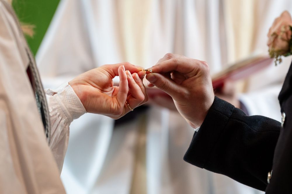 Close-up of couple exchanging wedding rings during marriage ceremony, hands holding gold band.