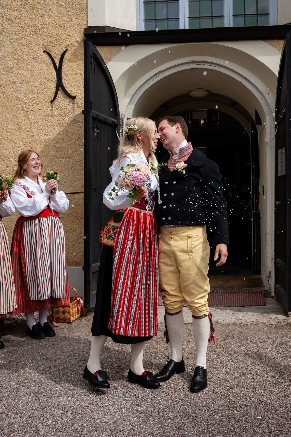 Couple in traditional Scandinavian folk costumes sharing a kiss outside a church door on their wedding day.