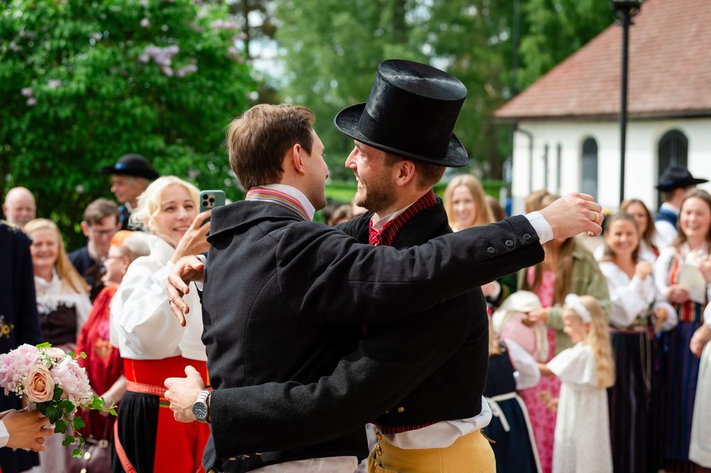 Two men in traditional Scandinavian folk costumes dance together outdoors at a festive cultural celebration.