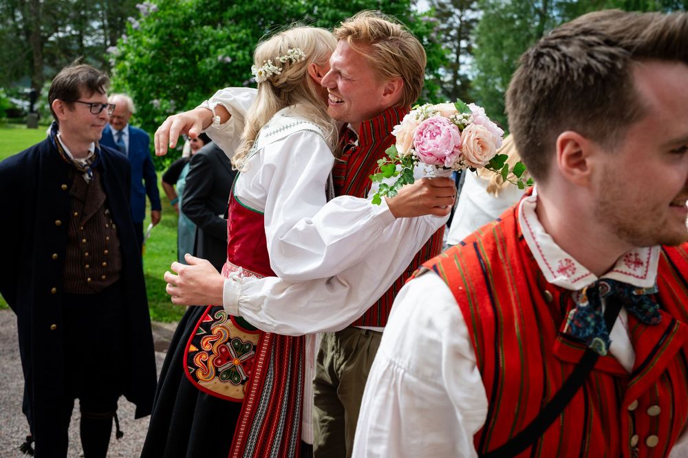 People wearing traditional Nordic folk costumes hugging and celebrating outdoors at a festive Scandinavian cultural gathering.