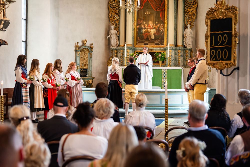 Traditional Norwegian church ceremony with people in bunad folk costumes gathered at the altar during a festive service.
