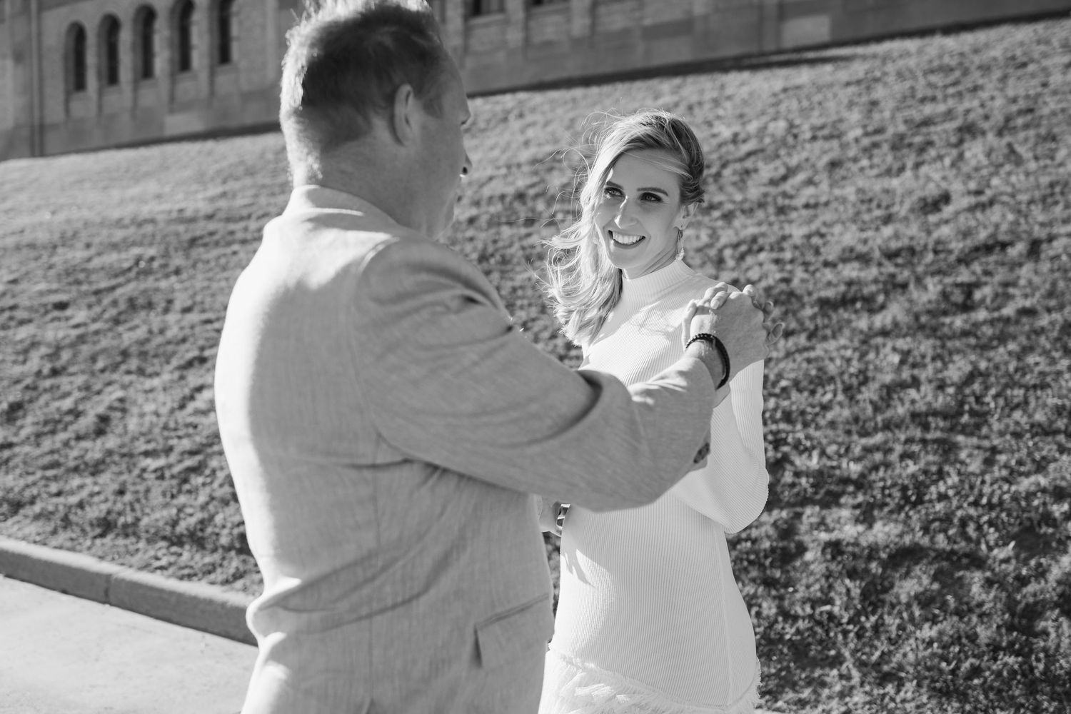 Black and white photo of a couple sharing a tender moment outdoors, woman smiling warmly at man in suit.