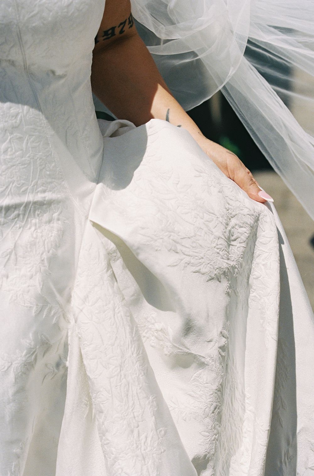 Close-up of a bride holding her white embroidered wedding gown with a flowing veil overhead.