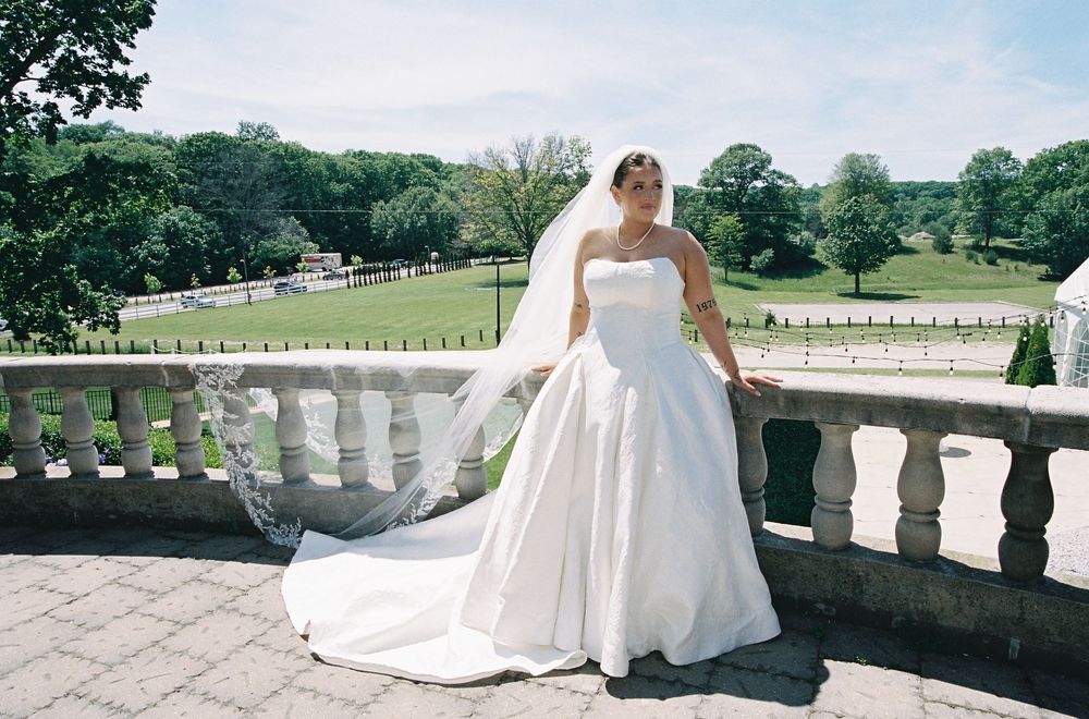 Beautiful bride in a strapless white ball gown with cathedral veil posing on a stone balcony at an estate venue.