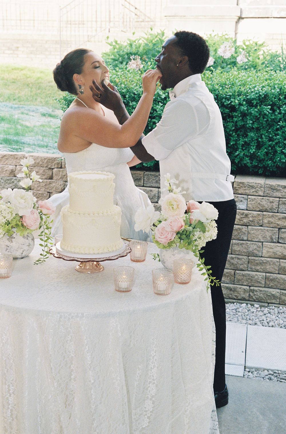 Bride and groom sharing a playful cake feeding moment at their elegant outdoor wedding reception.
