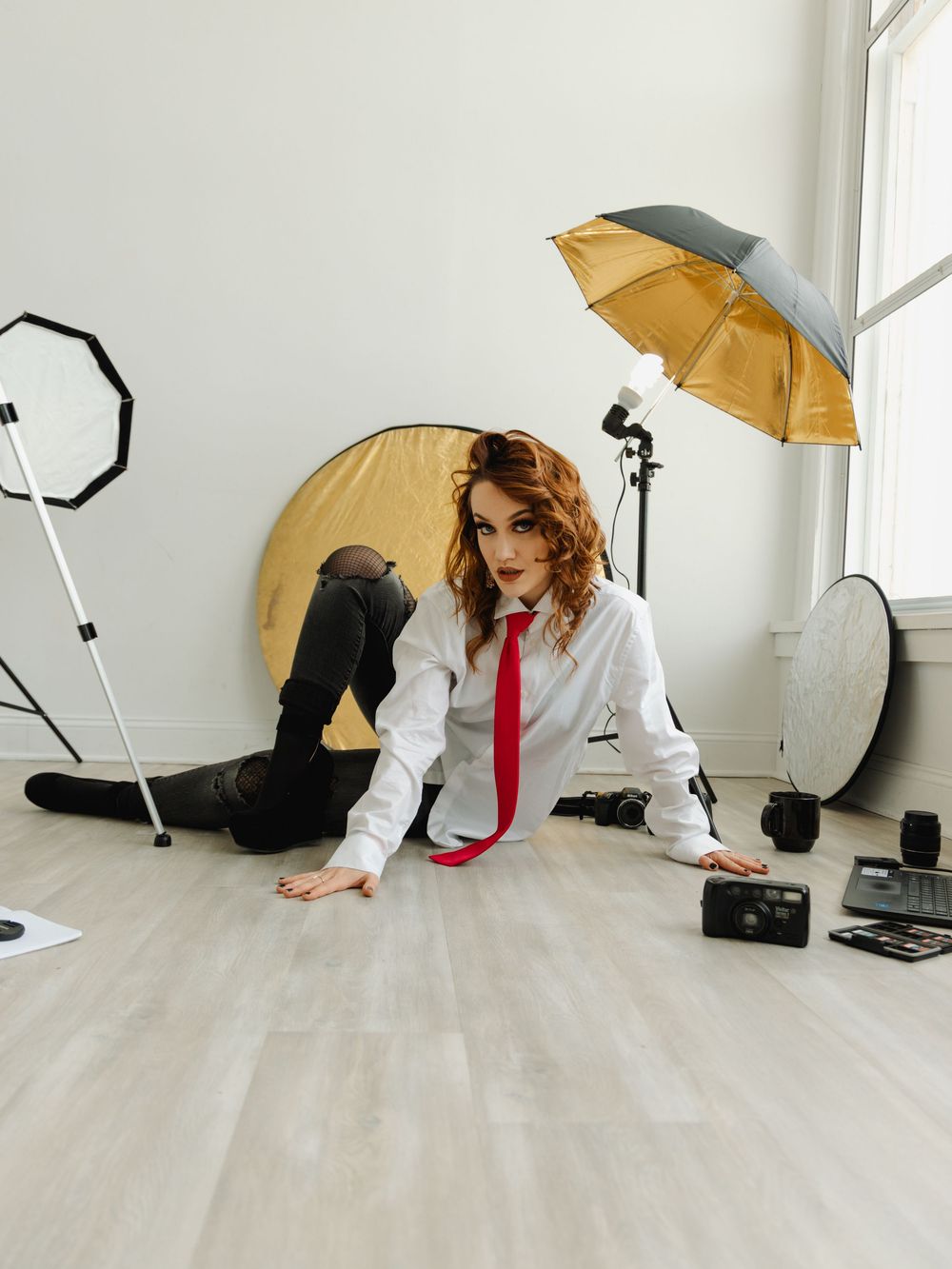 Woman wearing a button down shirt & tie, sitting on the floor in front of photography gear