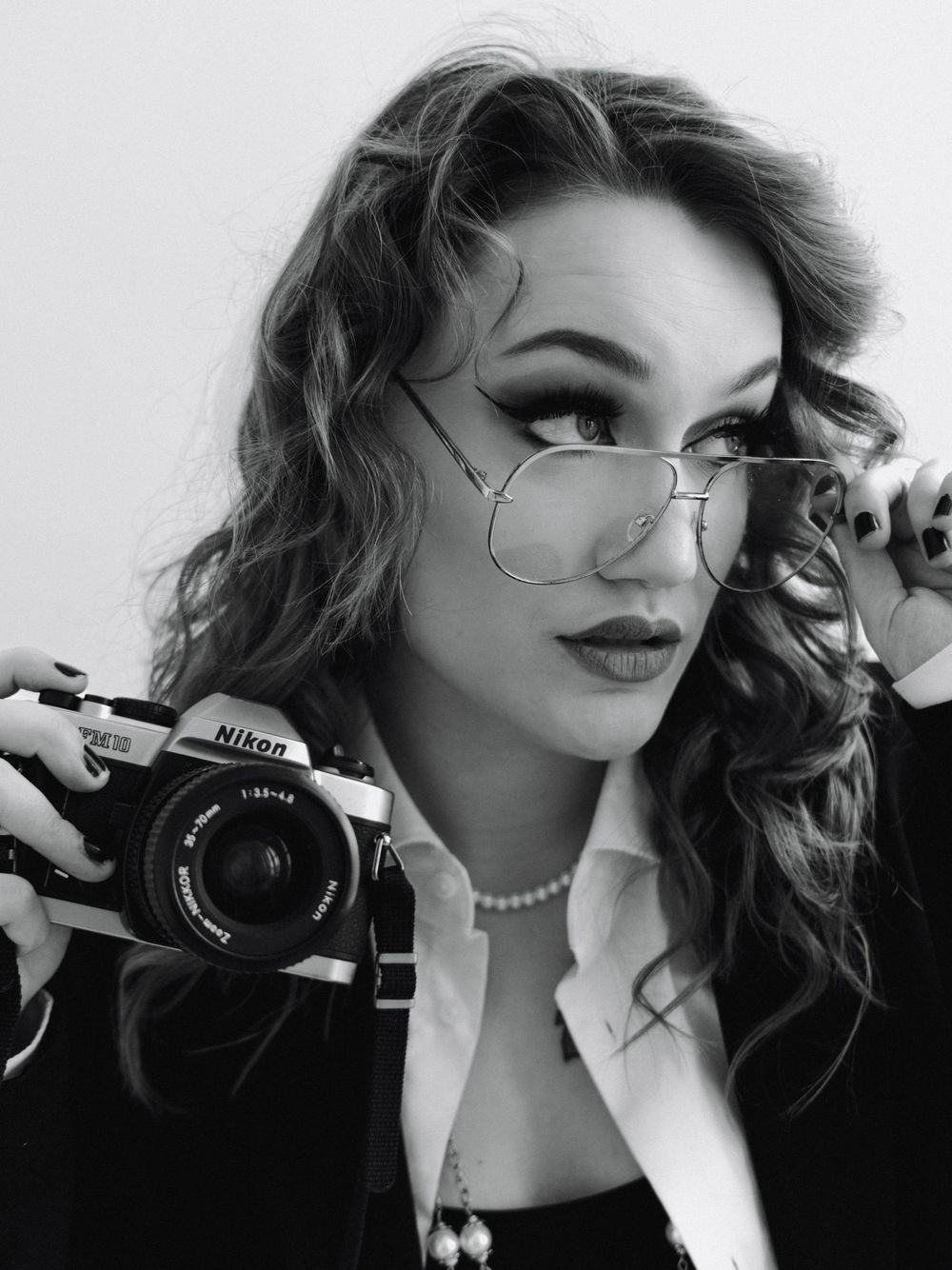 Woman wearing a business suit & reading glasses while holding a vintage camera