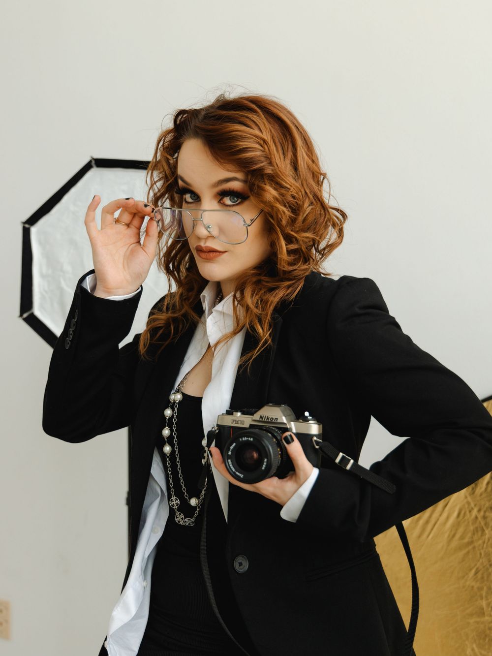 Woman wearing a business suit & reading glasses while holding a vintage camera