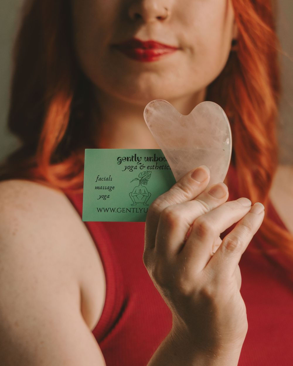Esthetician holding a rose quartz guah sha tool and a  business card in front of her face