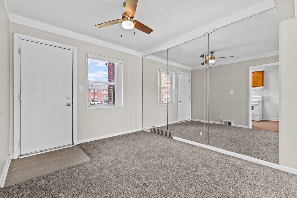Carpeted bedroom with mirrored closet doors, crown molding, ceiling fan, and natural window light.