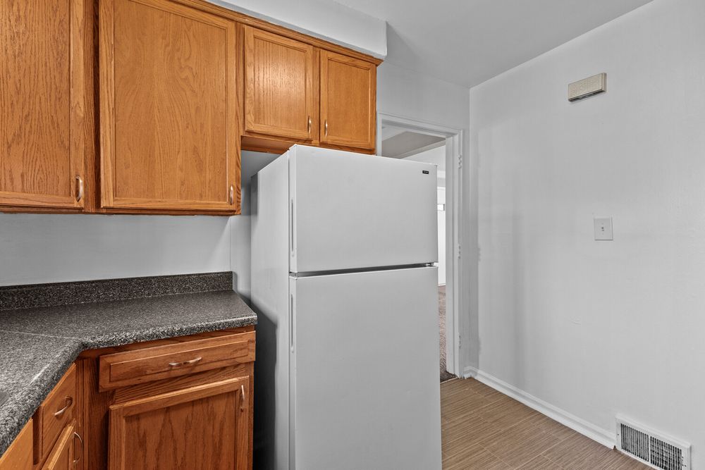 Kitchen with oak cabinets, dark granite countertops, and a white refrigerator on light hardwood floors.