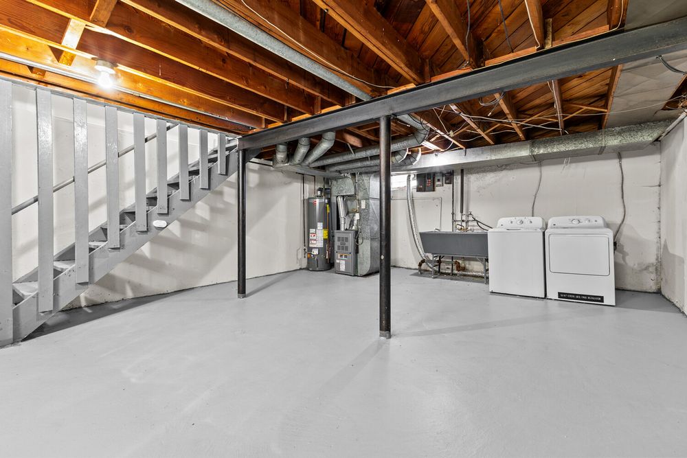 Unfinished basement laundry area with washer, dryer, water heater, painted floors, and open staircase.