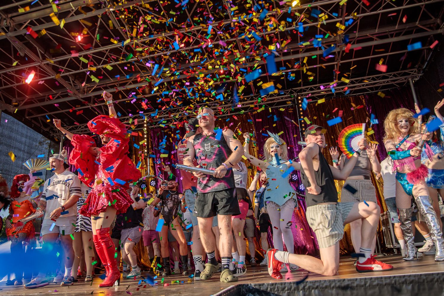Colorful confetti rains over performers in festive costumes celebrating Pride on a vibrant outdoor stage.