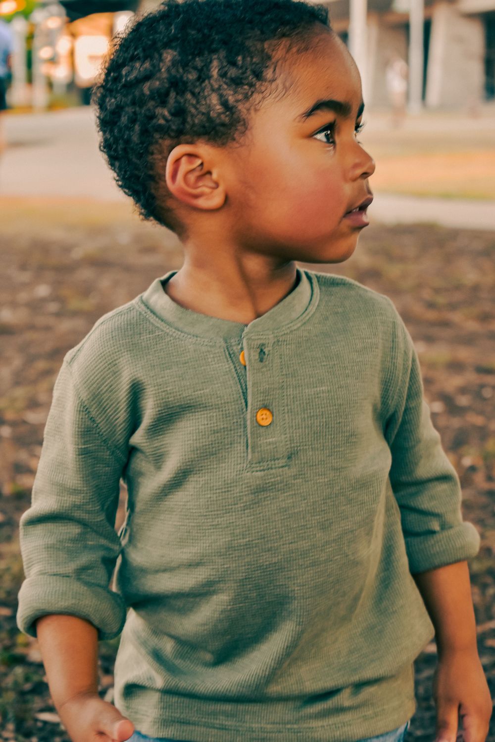 Cute young boy in a sage green henley sweater looking away outdoors in natural light.