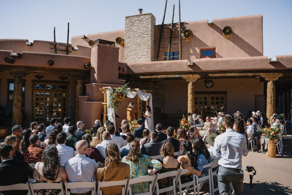 Outdoor wedding ceremony at Southwest adobe venue with guests seated in sunny courtyard.