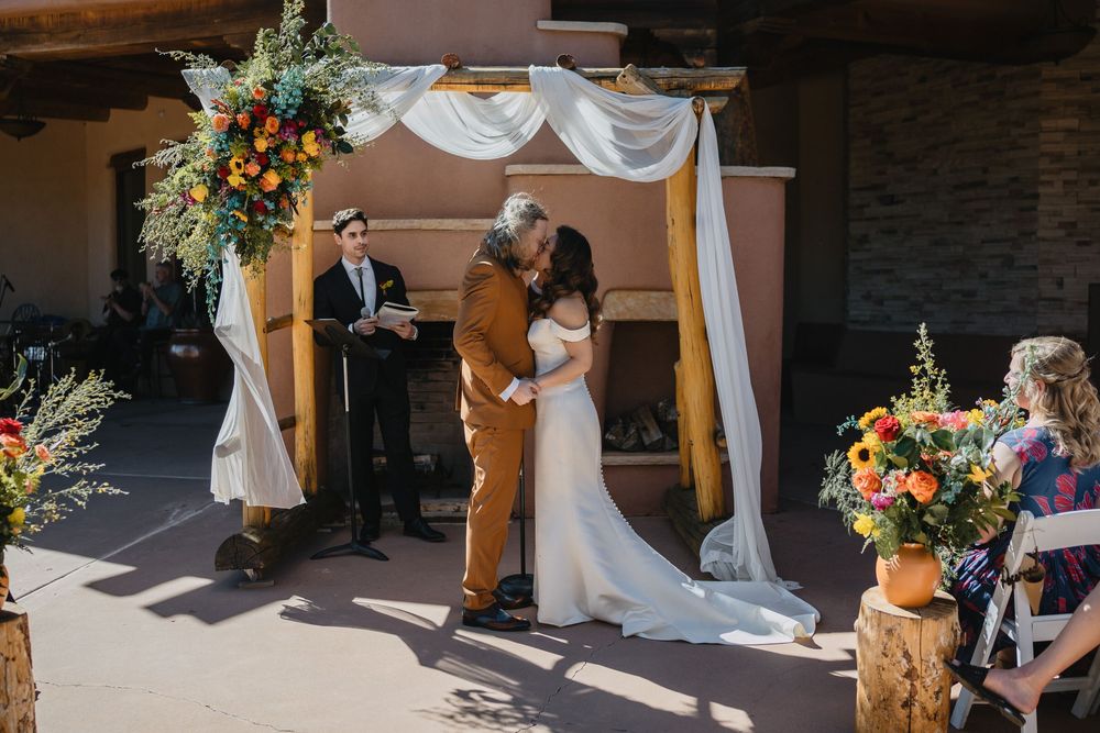 Bride and groom share first kiss under draped wooden arch at Southwest wedding ceremony at Nature Pointe venue