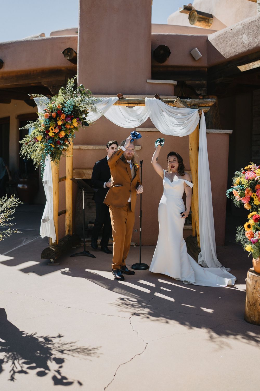 Joyful newlyweds celebrate after ceremony under floral arch at sunny Southwest wedding at Nature Pointe venue
