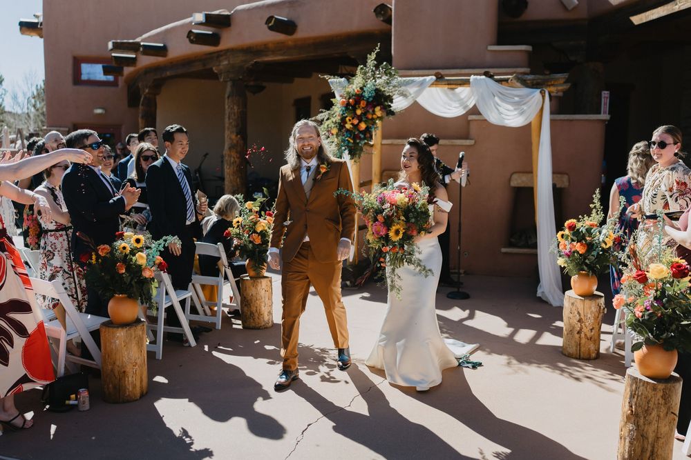 Newlyweds walk down the aisle at outdoor Southwest-style wedding venue with vibrant floral arrangements at Nature Pointe venue