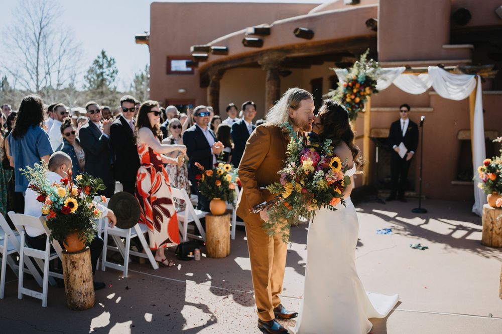 Bride and groom share a kiss at outdoor wedding ceremony with colorful floral arrangements on log pedestals at Nature Pointe venue