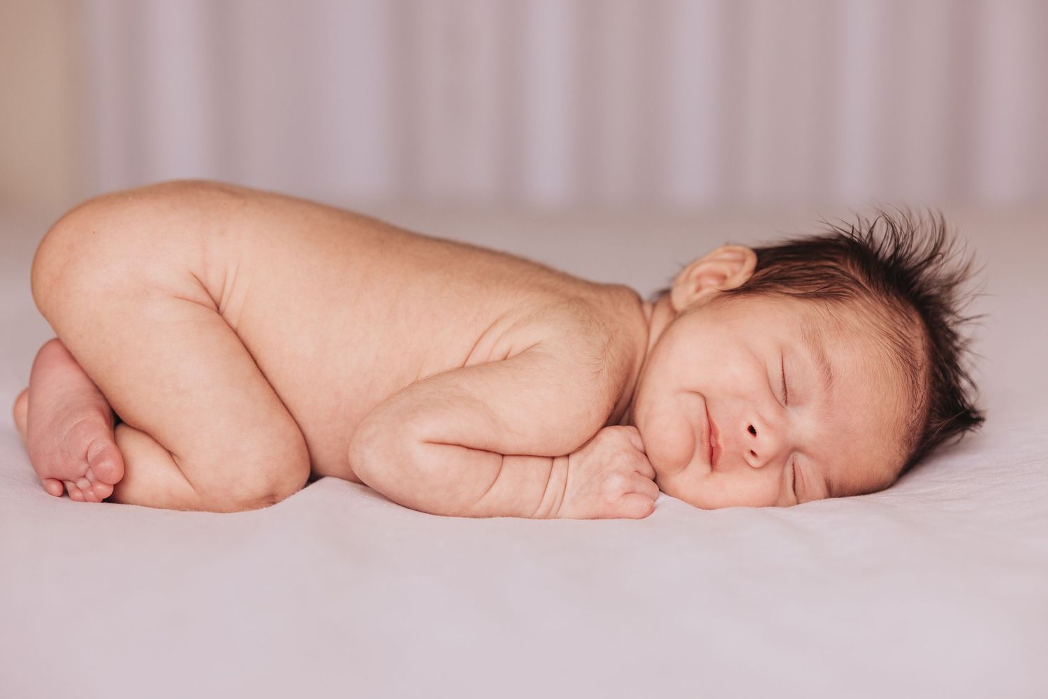 Sleeping newborn baby lying peacefully on soft pink backdrop.