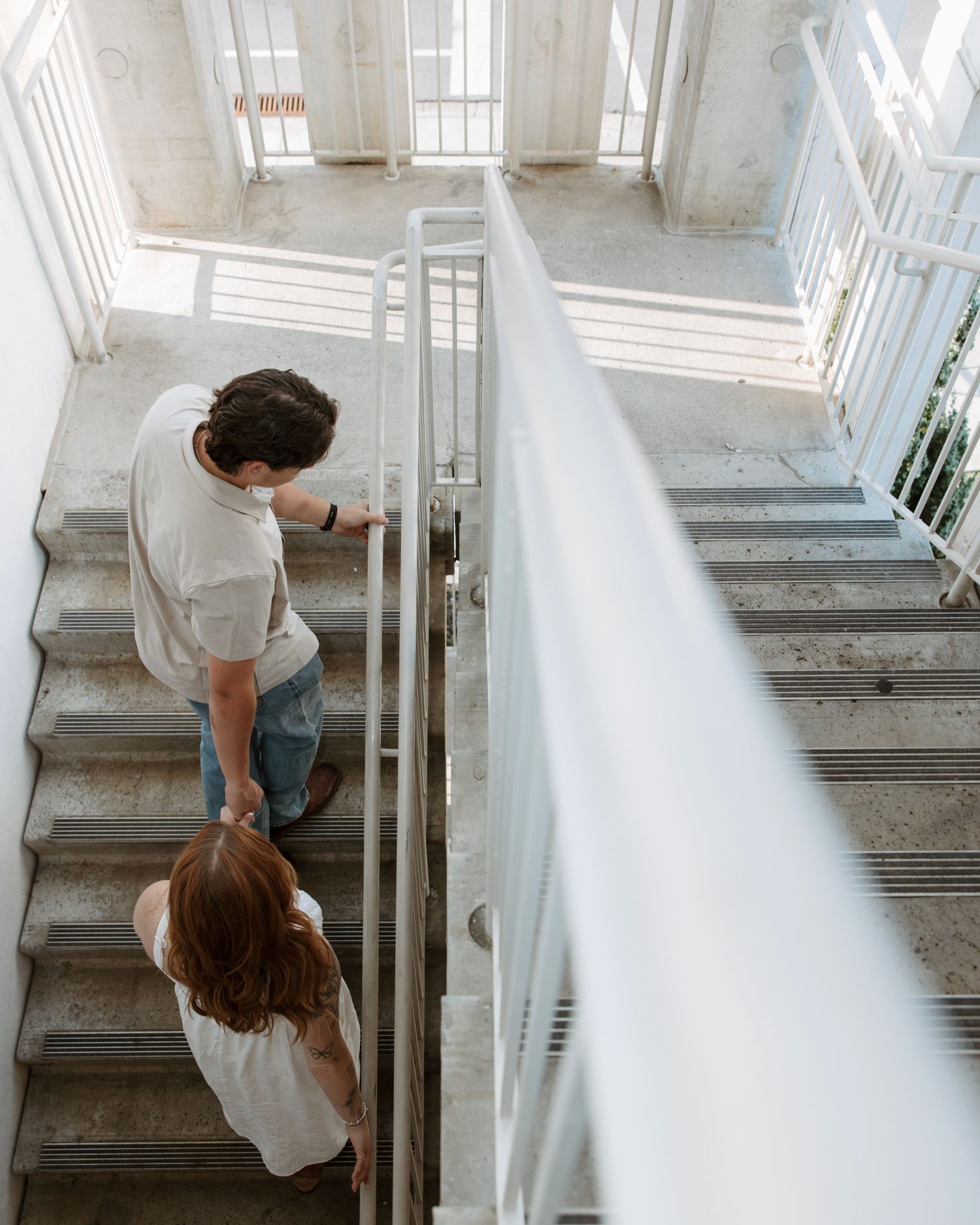 Couple holding hands while descending concrete staircase viewed from above.