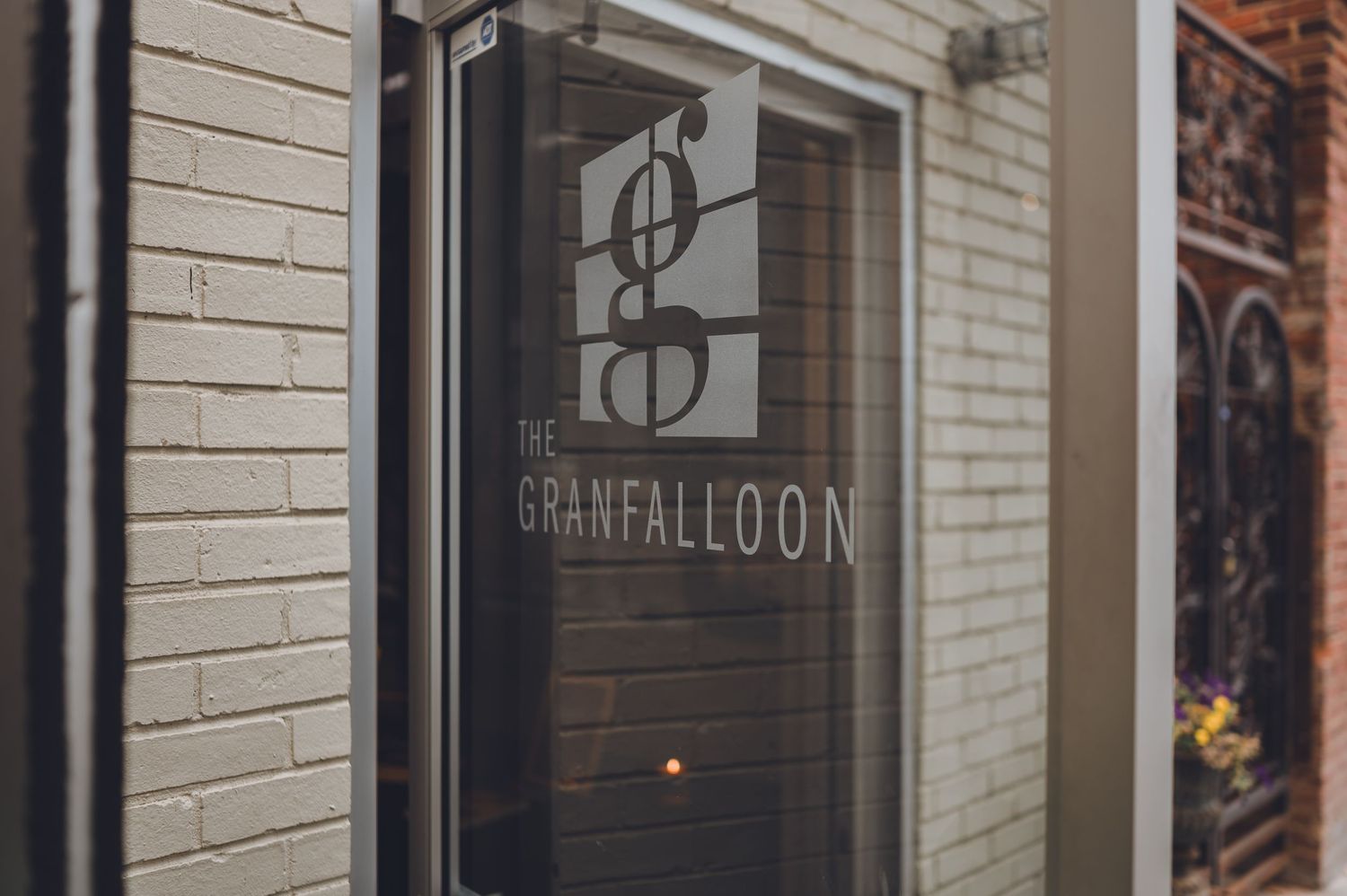 The Granfalloon restaurant entrance sign displayed on a glass door of a brick building.