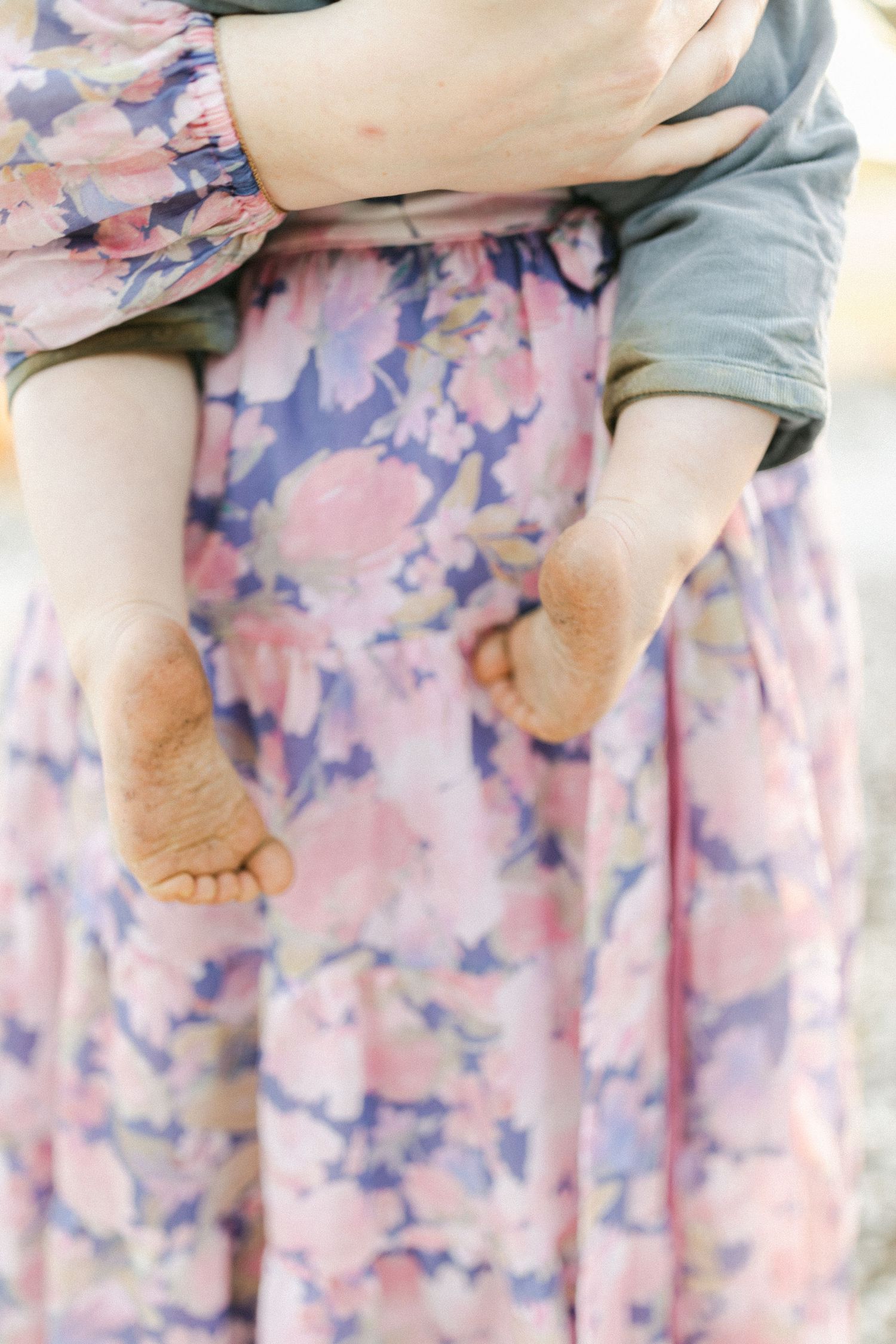 Close-up of a baby's bare feet dangling as mother holds infant against her pink floral dress.