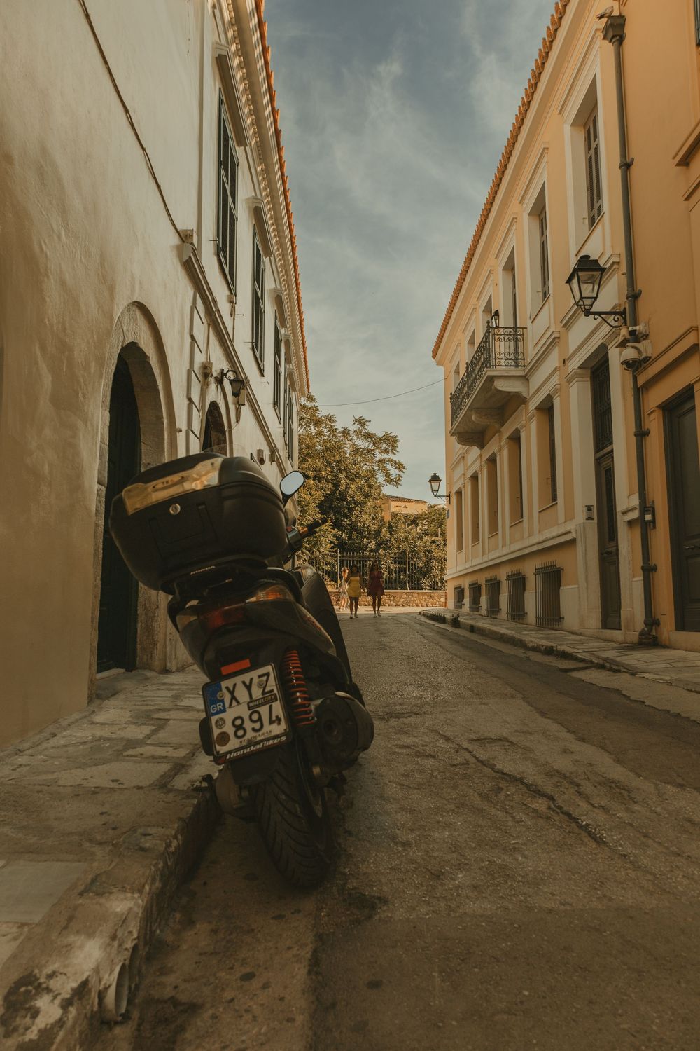 Vintage scooter parked on narrow cobblestone street between classical Greek buildings in Athens Greece.