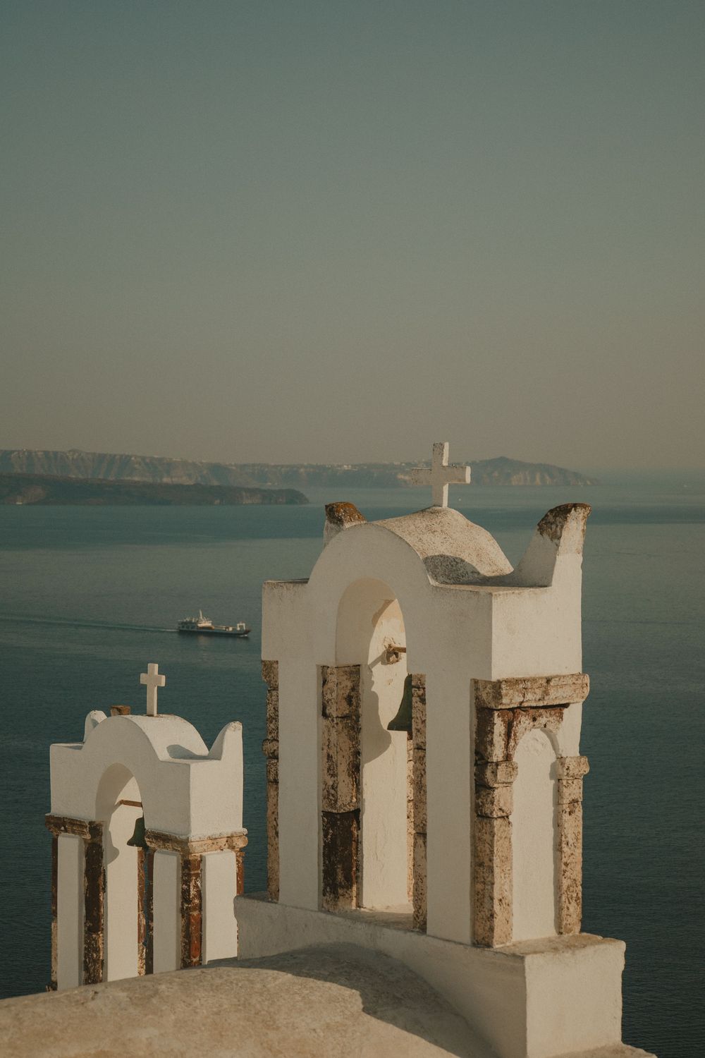 Ancient white Greek Orthodox bell towers with crosses and sea view in golden light Santorini Greece.