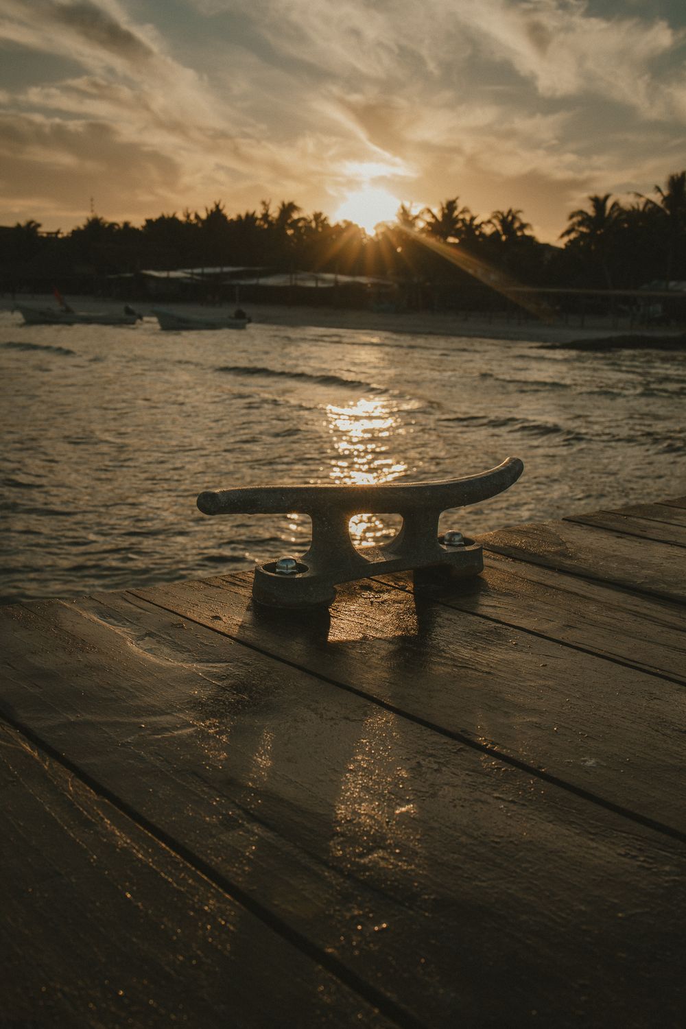 A boat cleat on a wooden dock silhouetted against a stunning tropical sunset over the ocean.