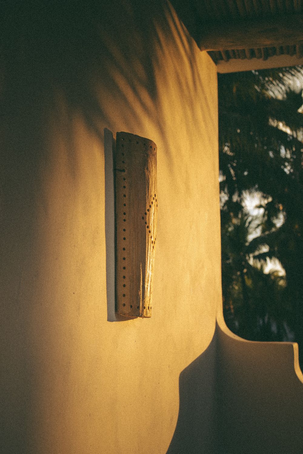 Decorative wooden wall sconce casting warm golden light on textured beige stucco wall outdoors.