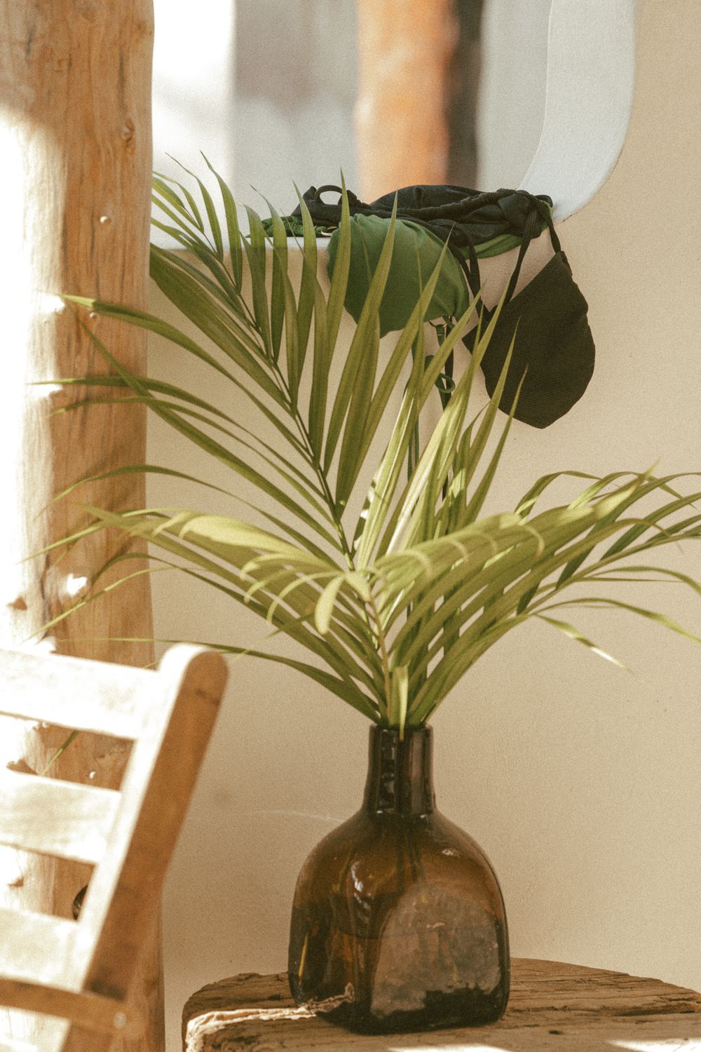 Green tropical palm leaves arranged in a dark glass bottle vase on a rustic wooden shelf.