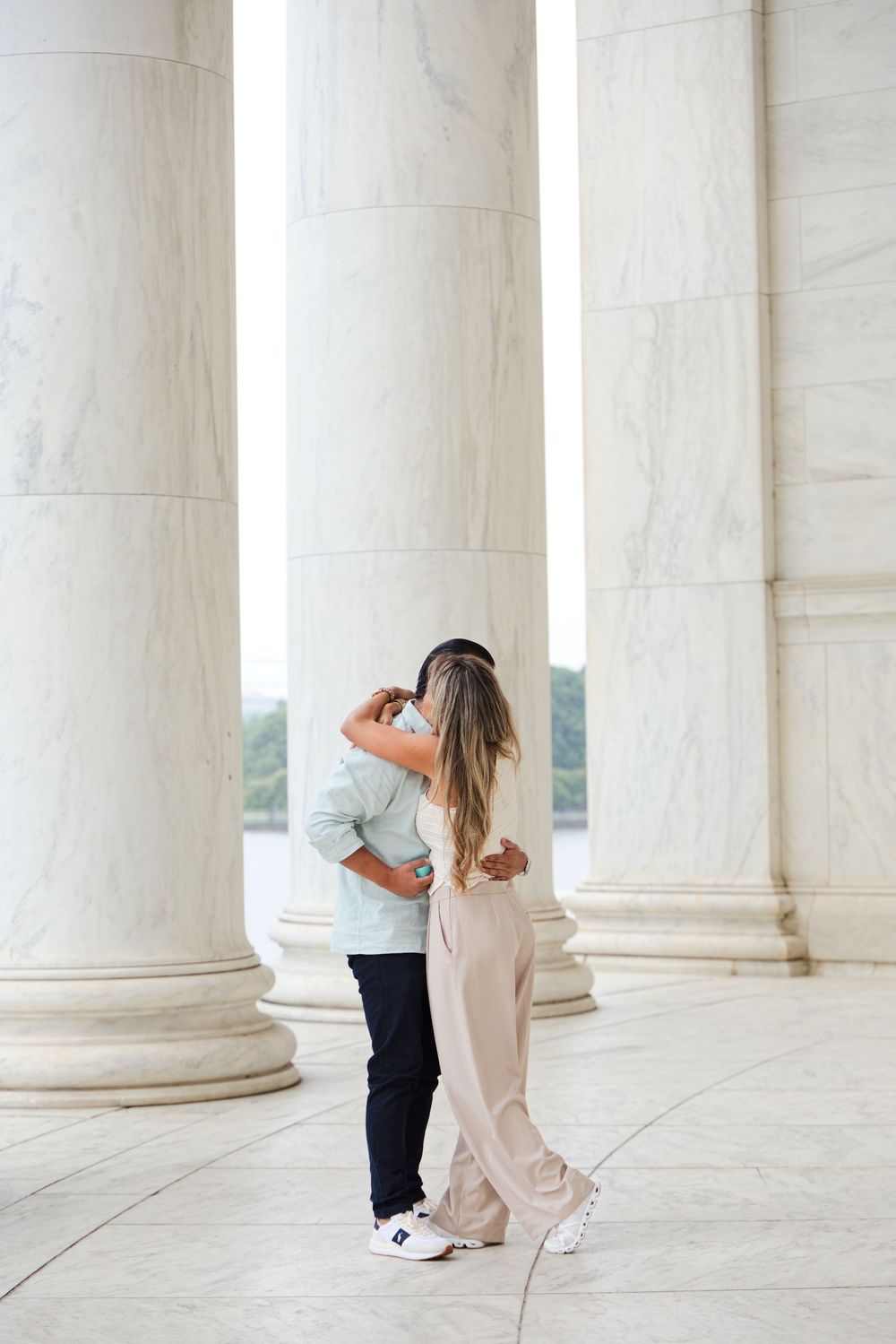Couple embracing and kissing between grand marble columns at the Jefferson Memorial in DC.