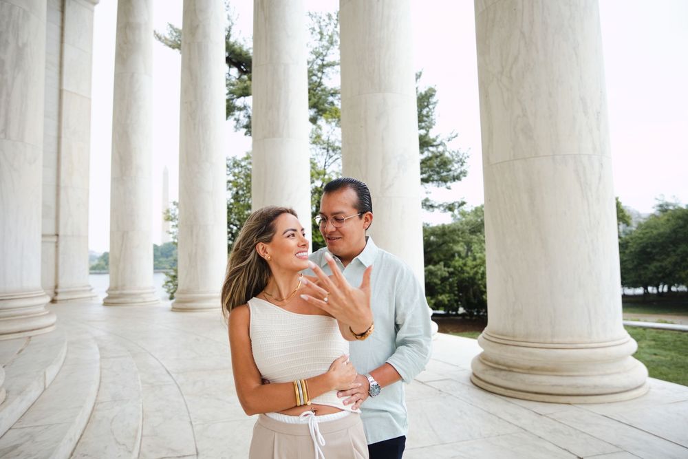 Couple embracing and smiling among white marble columns at the Jefferson Memorial in Washington, DC.