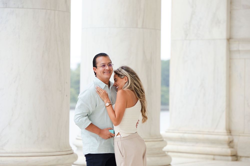 A smiling couple embraces between marble columns at the Jefferson Memorial in Washington DC.