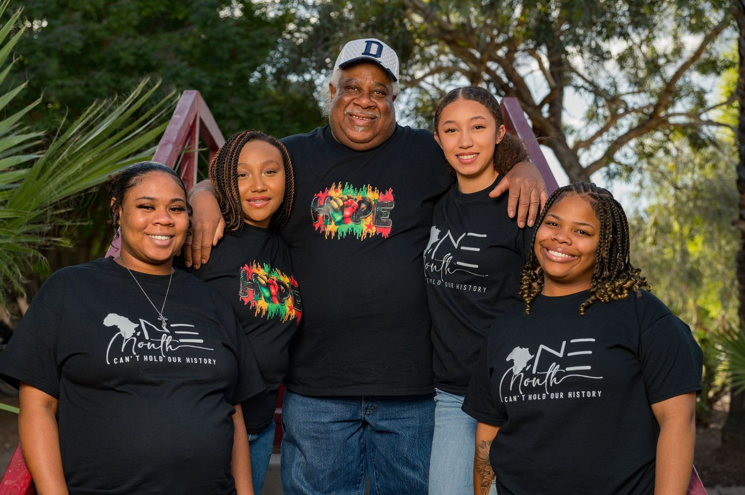 Family of five smiling together outdoors, wearing matching black ONE graphic t-shirts, posing for a group photo.