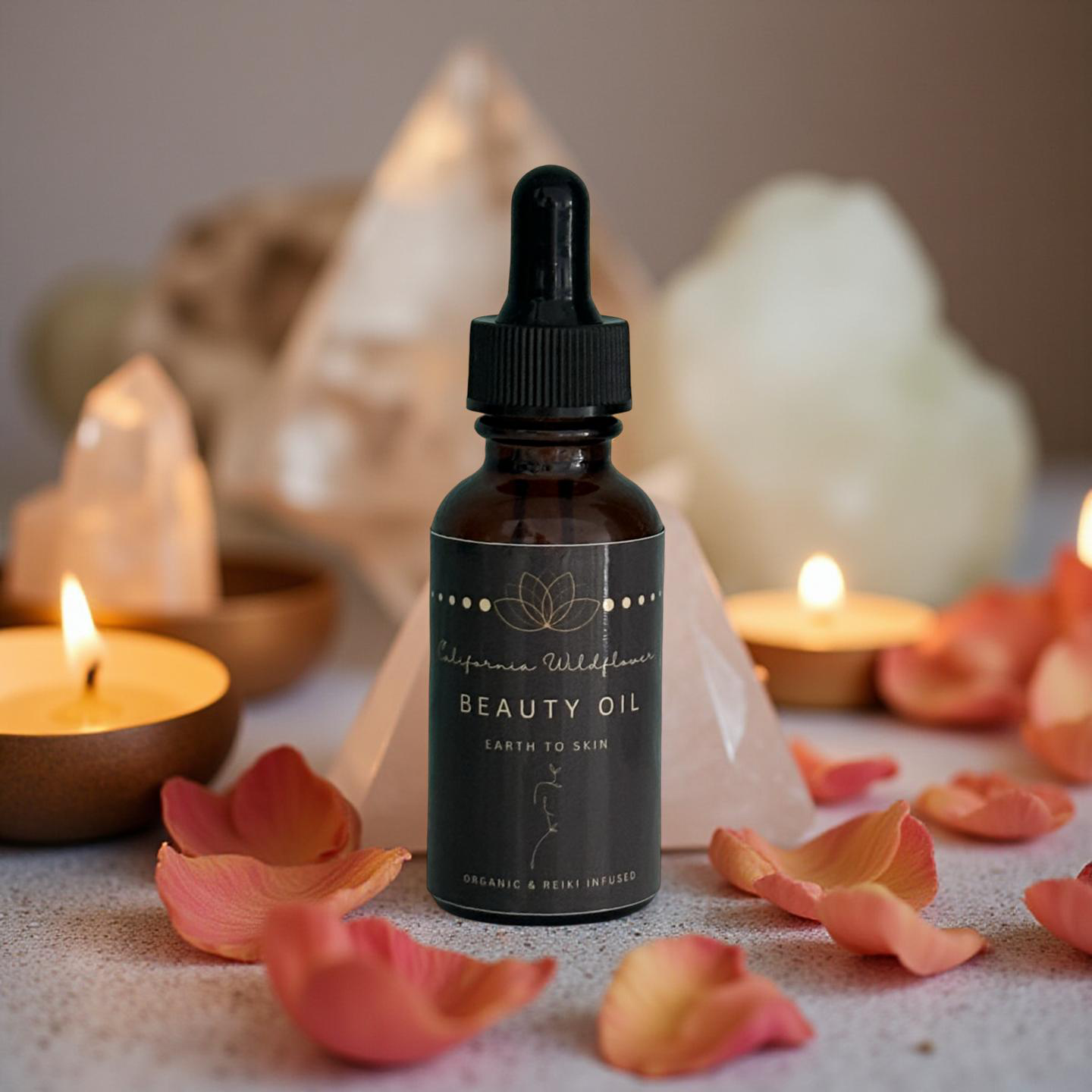 Amber dropper bottle of wildflower beauty oil surrounded by rose petals, crystals, and glowing candles on a serene surface.