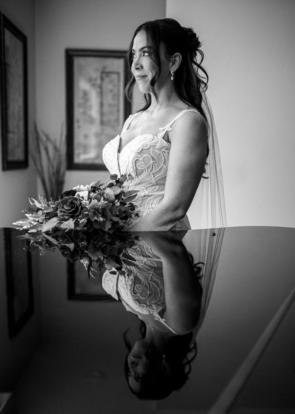 Black and white portrait of a bride holding a bouquet, with her reflection visible on a glass table.