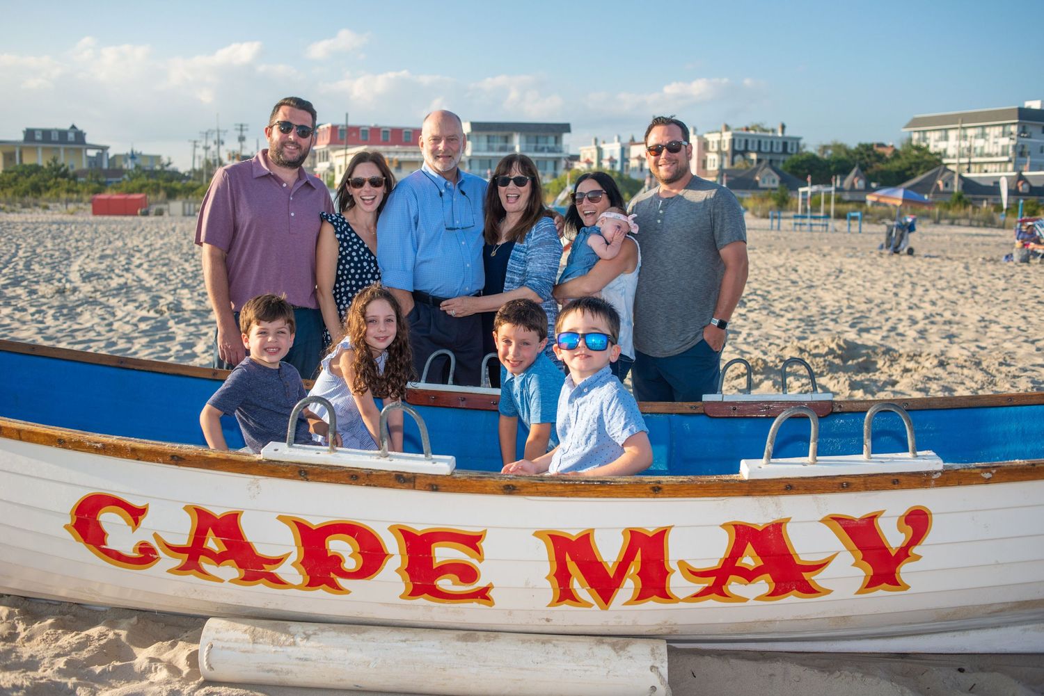 Family group photo at Cape May beach posing behind a colorful boat sign on a sunny day.