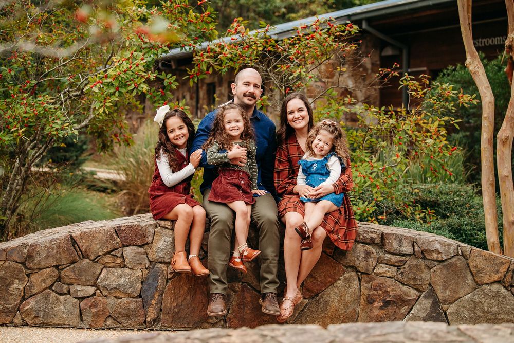 Happy family of five sitting on a stone wall surrounded by colorful autumn foliage.