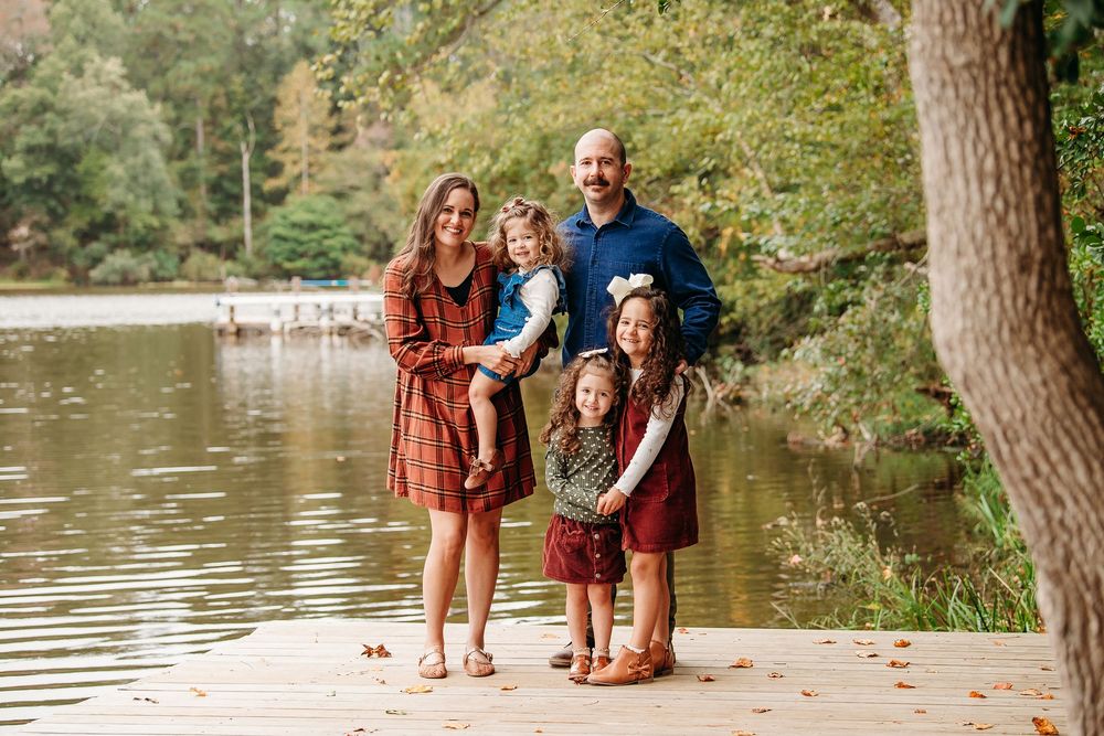 Family of five posing on a wooden dock beside a peaceful lake in autumn.